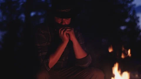 Cowboy plays the harmonica by a campfire at night in slow motion Stock-Footage 128779942