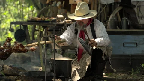 A cowboy preparing food at a rustic outdoor campfire Stock Footage 326210280
