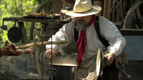 A cowboy preparing food at a rustic outdoor campfire Stock Footage 326210468