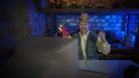 A cowboy in a straw hat plays a computer game with toy weapon in a garage. 스톡 동영상 329512014