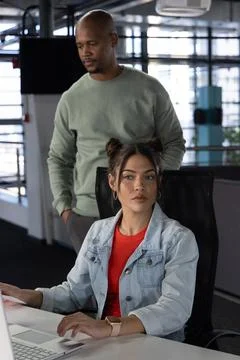 Coworkers collaborating at open-plan office with seated woman in denim jacket Stock Photos