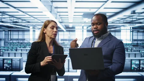 Coworkers in server room optimizing data center tech with laptop and tablet Stock Footage 277650985