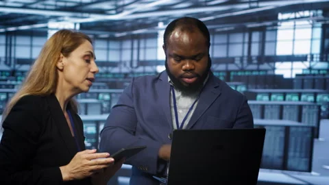 Coworkers in server room optimizing data center tech with laptop and tablet Stock Footage 277655030
