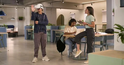 Coworkers in study area watching man donning VR headset, gesturing in VR demo Stock Footage 336658345