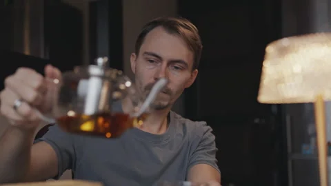 In a cozy atmosphere man pours himself tea at a table Stock Footage 294254261