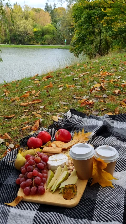 Cozy autumn picnic setup with coffee cups and fruits by lake. Video stock 344229086