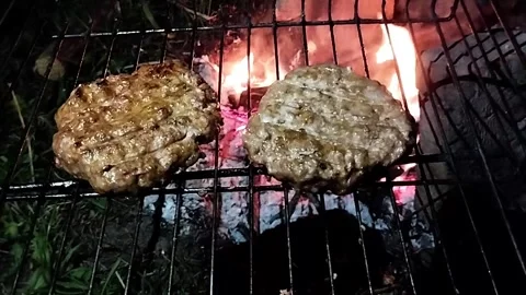 In a cozy backyard setting, two homemade burger patties sizzle on a grill above Stock Footage 292752354