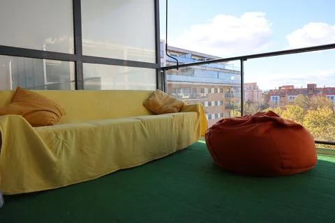 Cozy balcony seating area featuring a yellow sofa with cushions and an orange Stock Photos