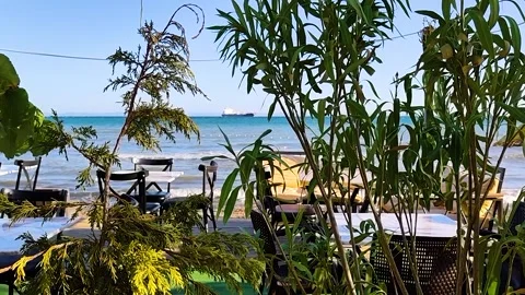 Cozy Beachside Cafe Tables and Chairs with a Cargo Ship on the Horizon Stock Footage 337415357