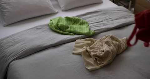 Cozy bed with casual assortment of clothes on it. consumer culture  Stock Footage 277970266