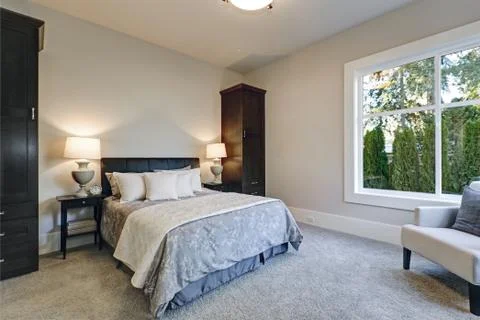 Cozy bedroom interior features soft creamy walls framing queen bed dressed in Stock Photos
