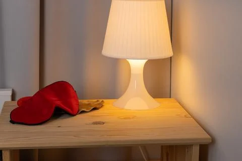 A cozy bedside table illuminated by a soft lamp, featuring a red blindfold, c Stock Photos