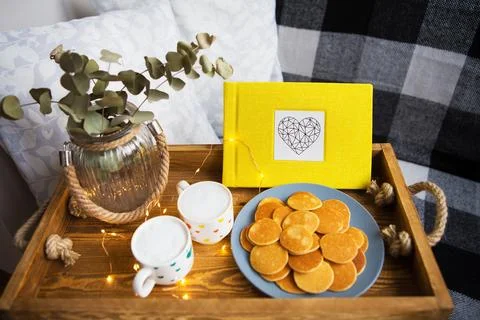 Cozy breakfast in bed scene with mini pancakes, coffee, and a yellow book o.. Stock Photos
