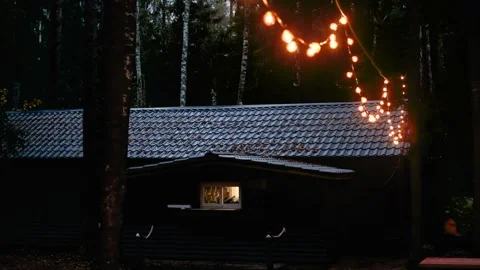 Cozy cabin illuminated by string lights at night with gradual camera zoom in Stock Footage 322070656