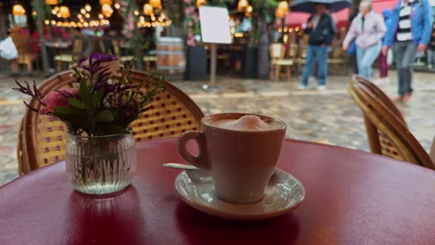Cozy Caf Table with Coffee and Flowers in a Bustling Outdoor Setting Stock Footage 318554514