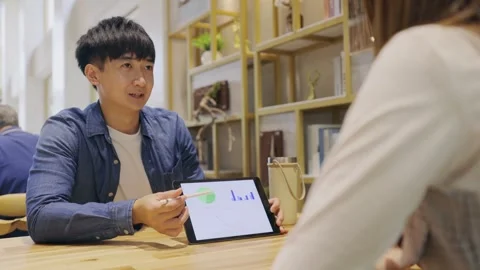 In a cozy cafe setting, two young entrepreneurs engage in a lively discussion Stock Footage 247039490