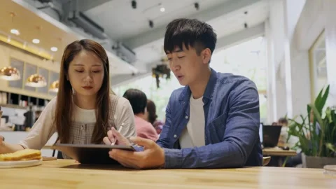 In a cozy cafe setting, two young entrepreneurs engage in a lively discussion Stock Footage 247040866