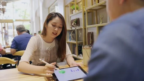 In a cozy cafe setting, two young entrepreneurs engage in a lively discussion Stock Footage 247041742