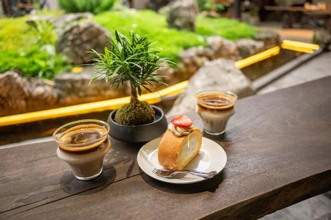 Cozy Cafe Table With Coffee Cups, Strawberry Roll Cake and Bonsai Plant Stock Photos