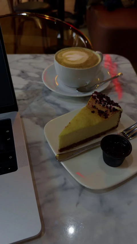Cozy cafe table with latte, cake slice, and laptop beside marble surface in warm Stock Footage 344966473