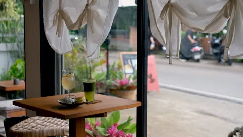 Cozy café table with refreshing drinks and a scone pastry beside a large window 스톡 동영상 341684669