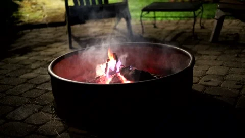 Cozy campfire in metal firepit on stone patio with orange flames flickering Stock Footage 325889756