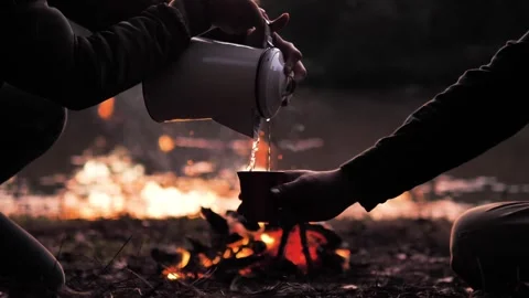 Cozy campfire at night with two people sharing hot drink Stock Footage 335899073