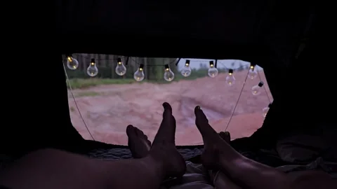 Cozy camping scene from rooftop tent with string lights, resting legs in nature Stock Footage 333129043