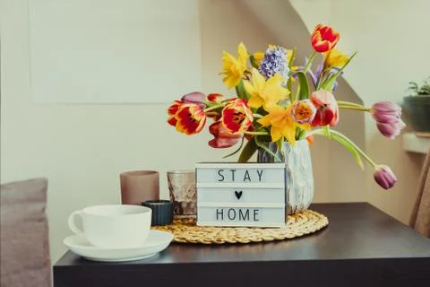 Cozy composition of cup of tea, lightbox with Stay home message and bouquet o Stock-Fotos