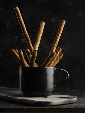 Cozy composition. On a dark background, a black cup with fragrant cinnamon st Stock Photos