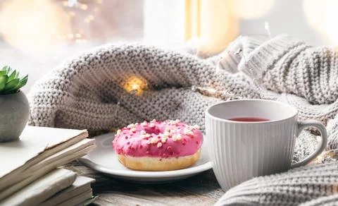 Cozy composition with a donut, a cup of tea and a knitted element. Stock Photos