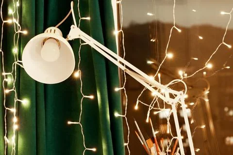 Cozy creative workspace with adjustable white desk lamp, warm string lights.. Stock Photos