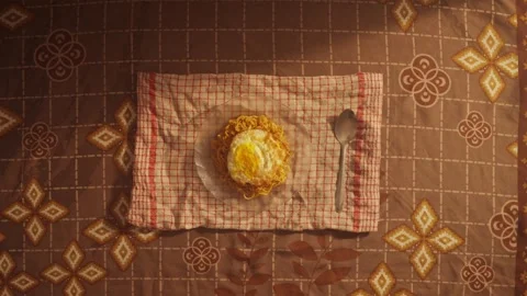 Cozy dining setup featuring noodles and a fried egg on a patterned tablecloth Stock Footage 297650634