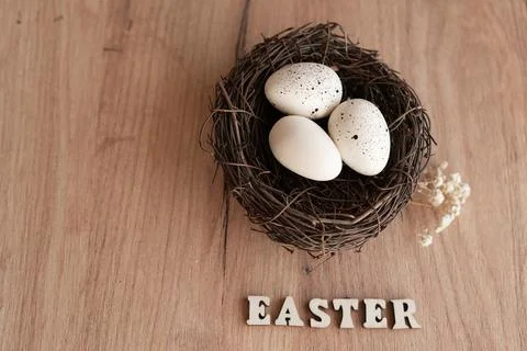 A cozy Easter nest filled with white and speckled eggs sits on a wooden sur.. Stock Photos