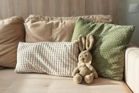 Cozy Easter scene featuring plush bunny on sofa with textured pillows. Stock Photos