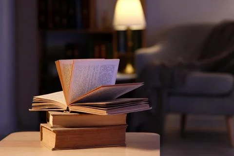 Cozy evening reading with open book on stack of old books, warm lamp light in Stock Photos