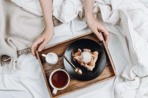 Cozy flatlay of bed, woman's hands holding wooden tray with vegan apple pie,  Stock Photos