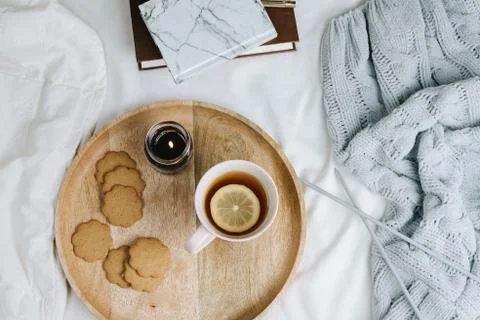 Cozy flatlay of cup of lemon tea on wooden tray in bed with knitted sweater,  Stock Photos