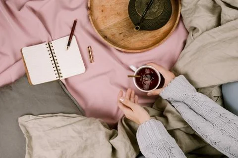 Cozy flatlay of woman's hands in bed with cup of tea, selective focus Stock Photos