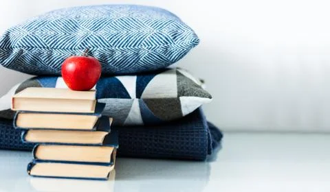 Cozy home interior decor: stack of books, red apple and blue pillows on a whi Stock Photos