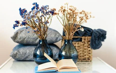 Cozy home interior decor: stack of books, vase with flowers, pillows and plai Stock Photos