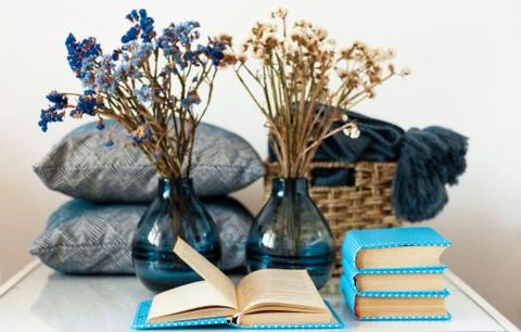 Cozy home interior decor: stack of books, vase with flowers on a white table. Stock Photos