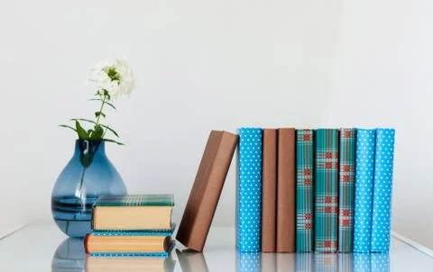 Cozy home interior decor: stack of books and vase with white flower on a glas Stock Photos
