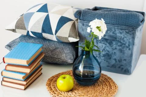 Cozy home interior decor: stack of books, green apple, decorative pillows, bo Stock Photos