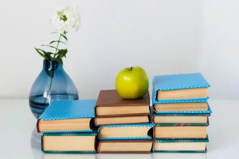 Cozy home interior decor: stack of books, green apple and vase with white flo Stock Photos