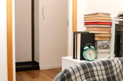Cozy home interior with a stack of books and a turquoise alarm clock on a w.. Stock Photos