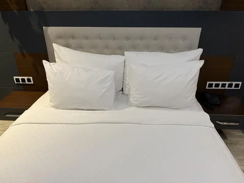 Cozy hotel bed with soft white pillows and sheets, offering a comfortable a.. Stock Photos