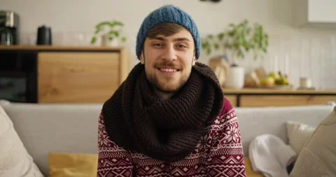 Cozy indoor setting features a smiling man in winter clothing knitting while Video stock 308388103