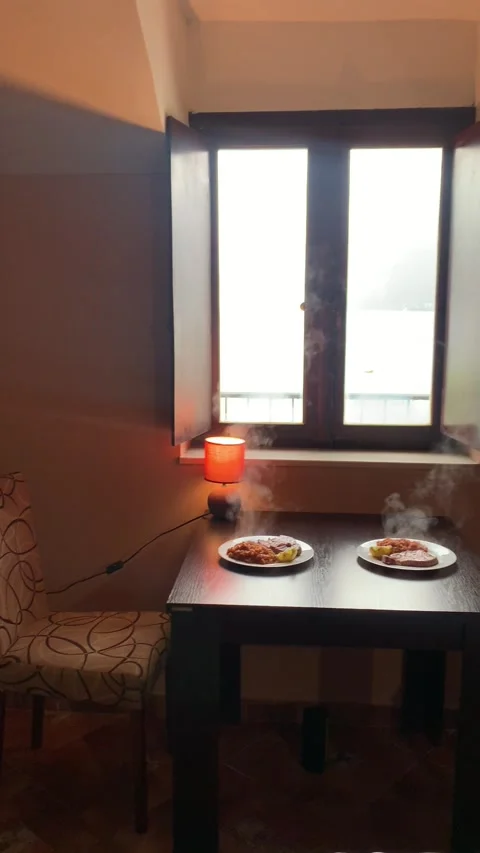 A cozy interior scene with a table set for two, featuring steaming plates of foo Stock Footage 296284639