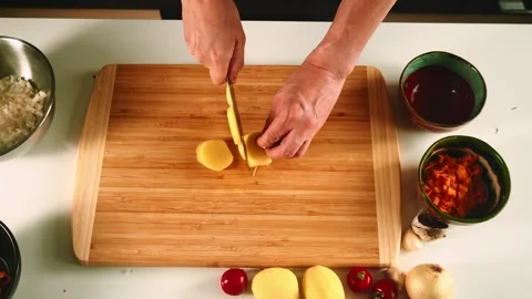 In a cozy kitchen, a person skillfully chops fresh vegetables on a wooden Stock-Footage 316635467